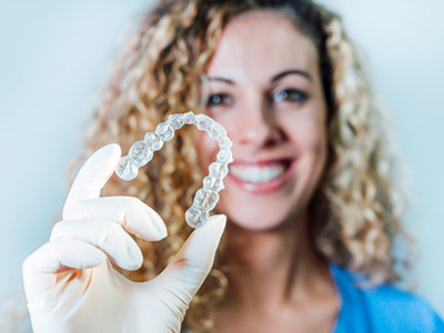 A woman wearing a blue shirt and holding up a clear dental retainer with her right hand.